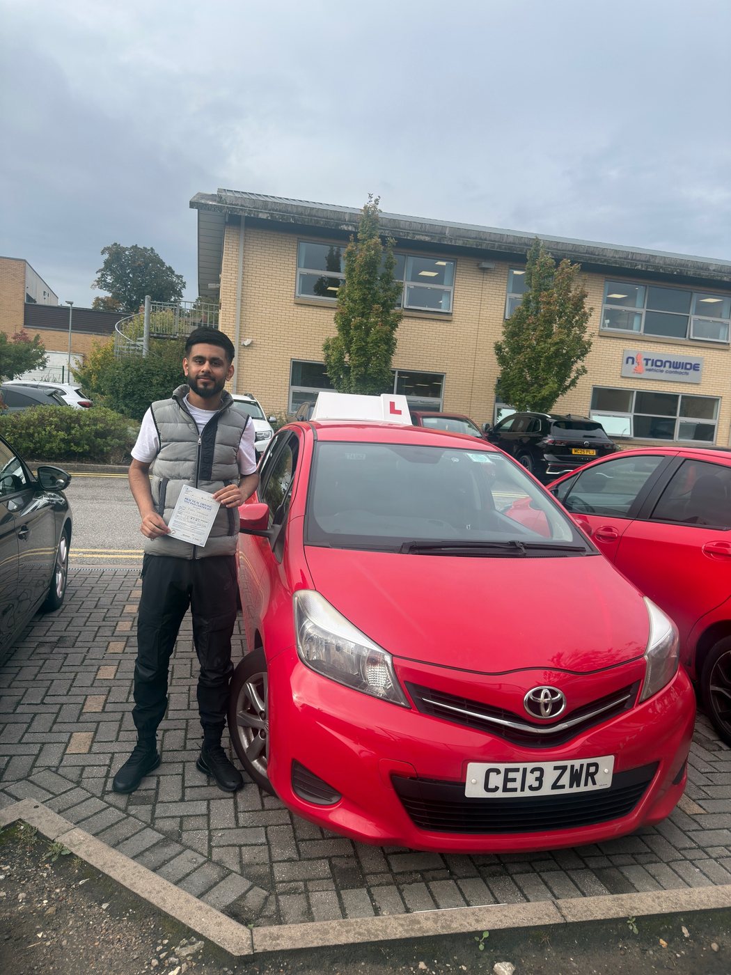 Student celebrating a driving test pass with learner car